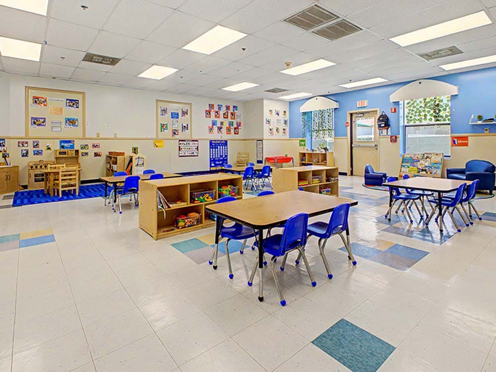 Classroom with small tables and chairs, play kitchen, and colorful floor tiles