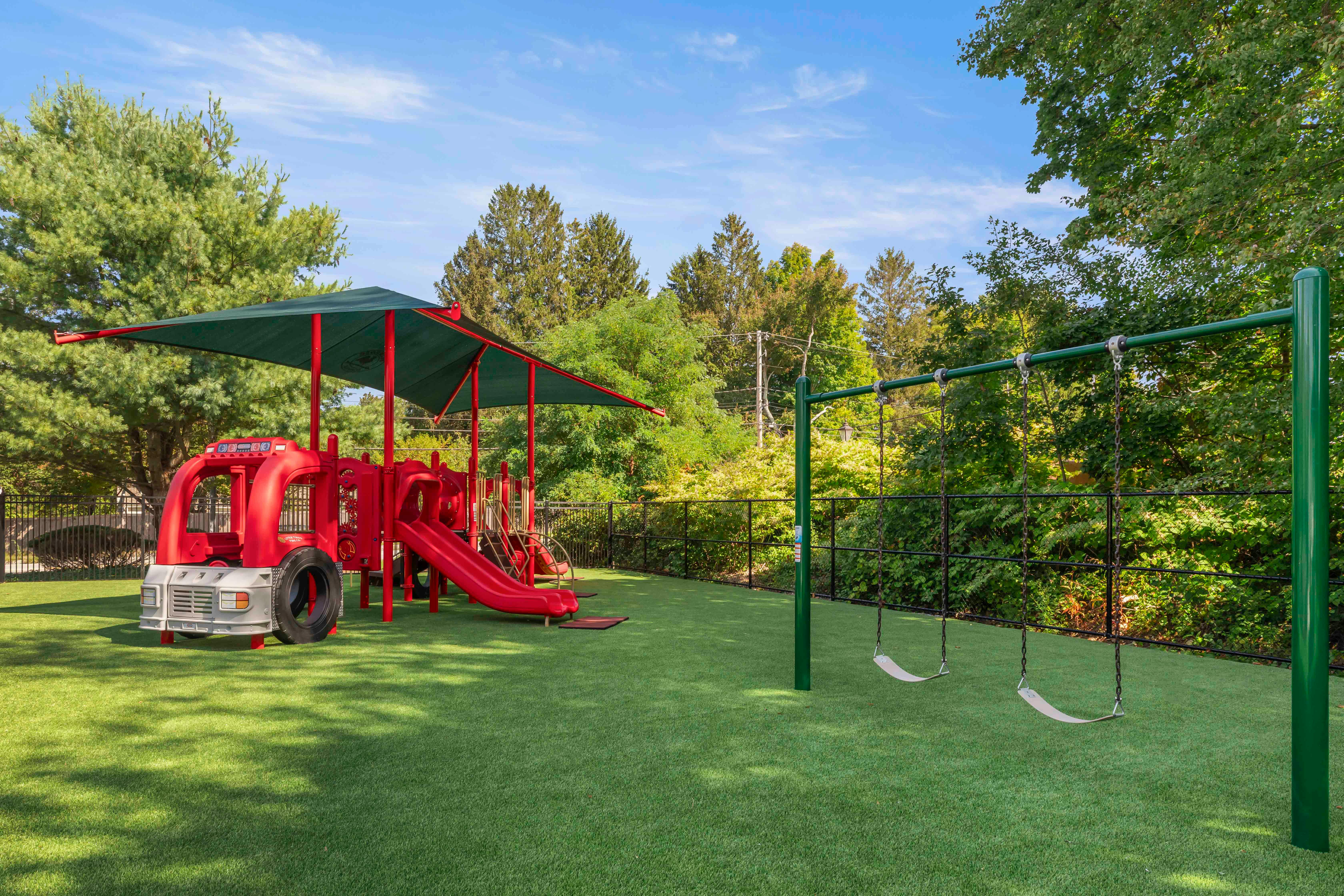 Playground with red fire truck climbing structure, slides, and swings on green turf