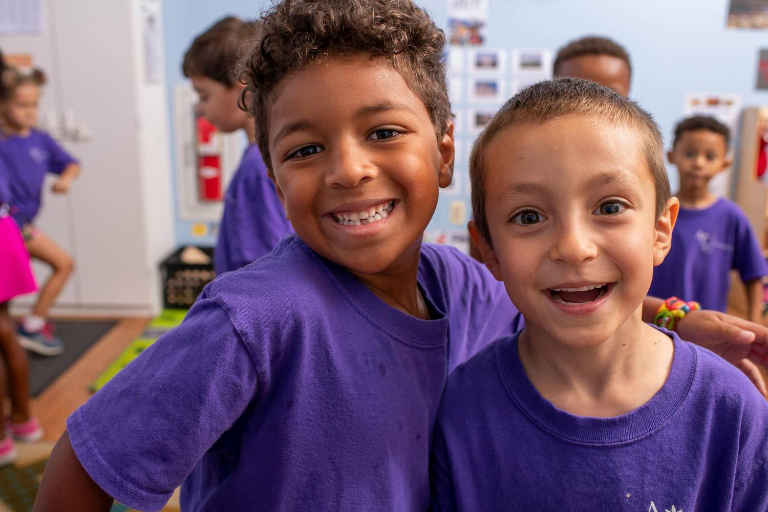 Two children in purple shirts smiling at the camera
