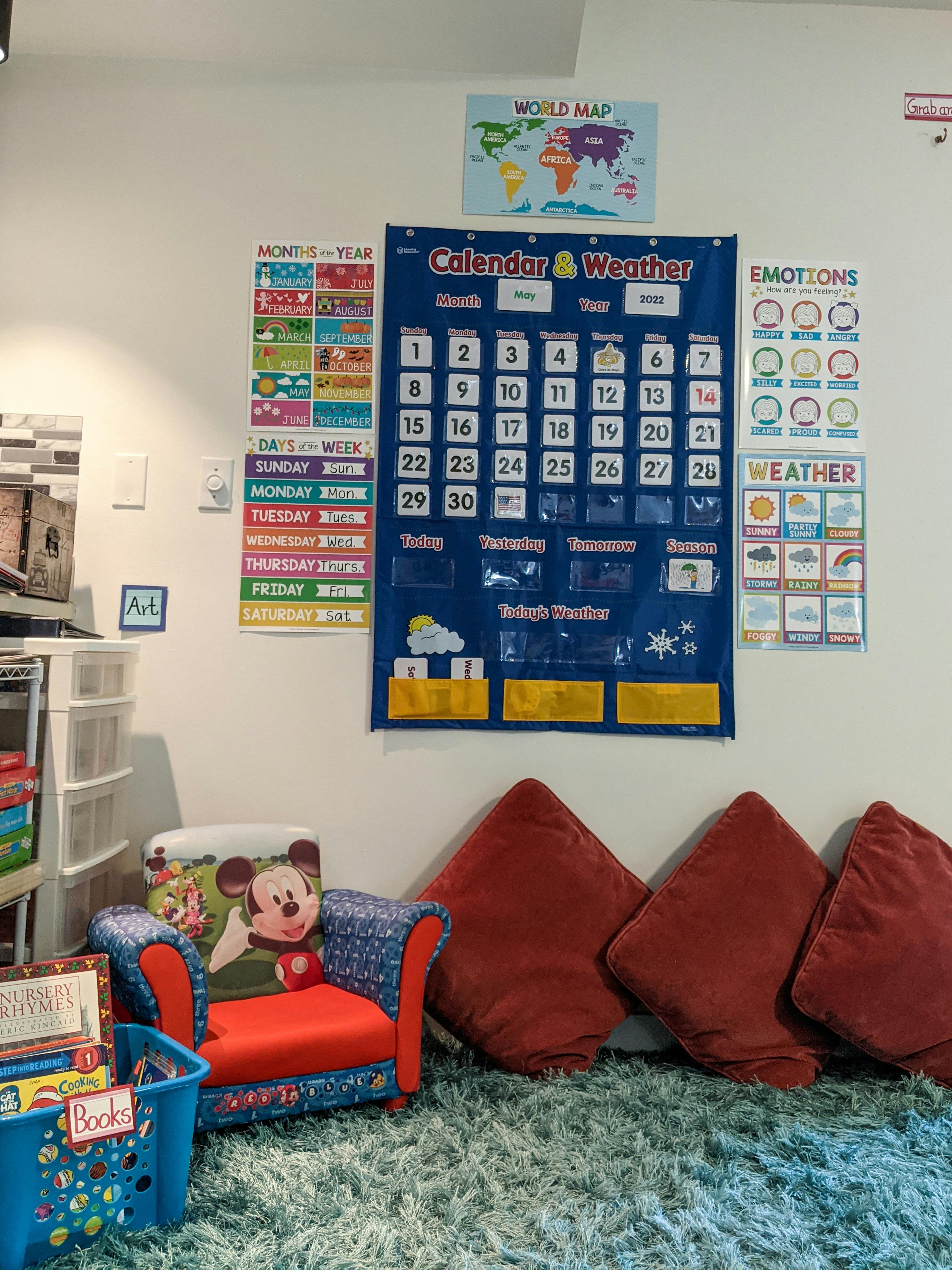Calendar and weather chart on a wall above a child's chair and pillows