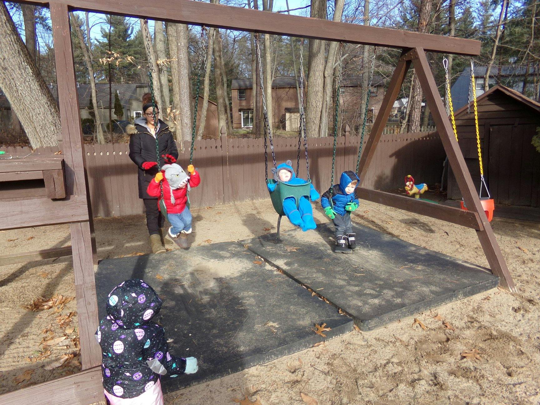Person pushing a child on a swing, two other children nearby