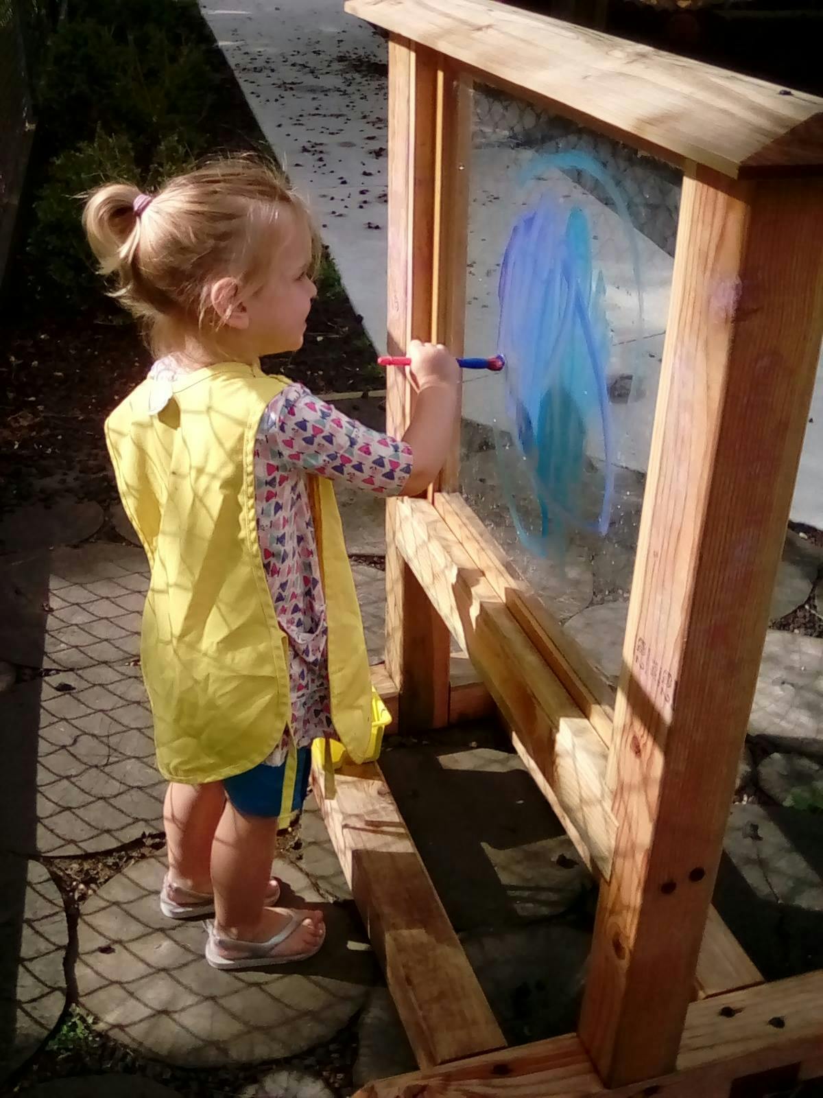 Child painting on a clear easel outdoors