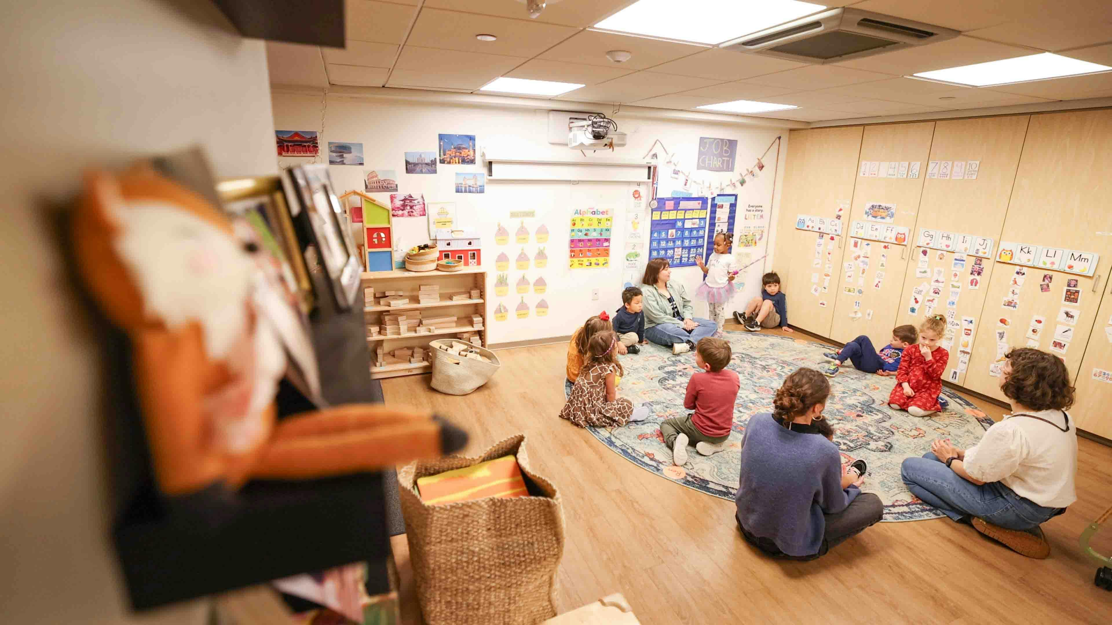 adults and children sitting on a rug in a classroom