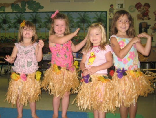 Four children in grass skirts and floral tops dancing