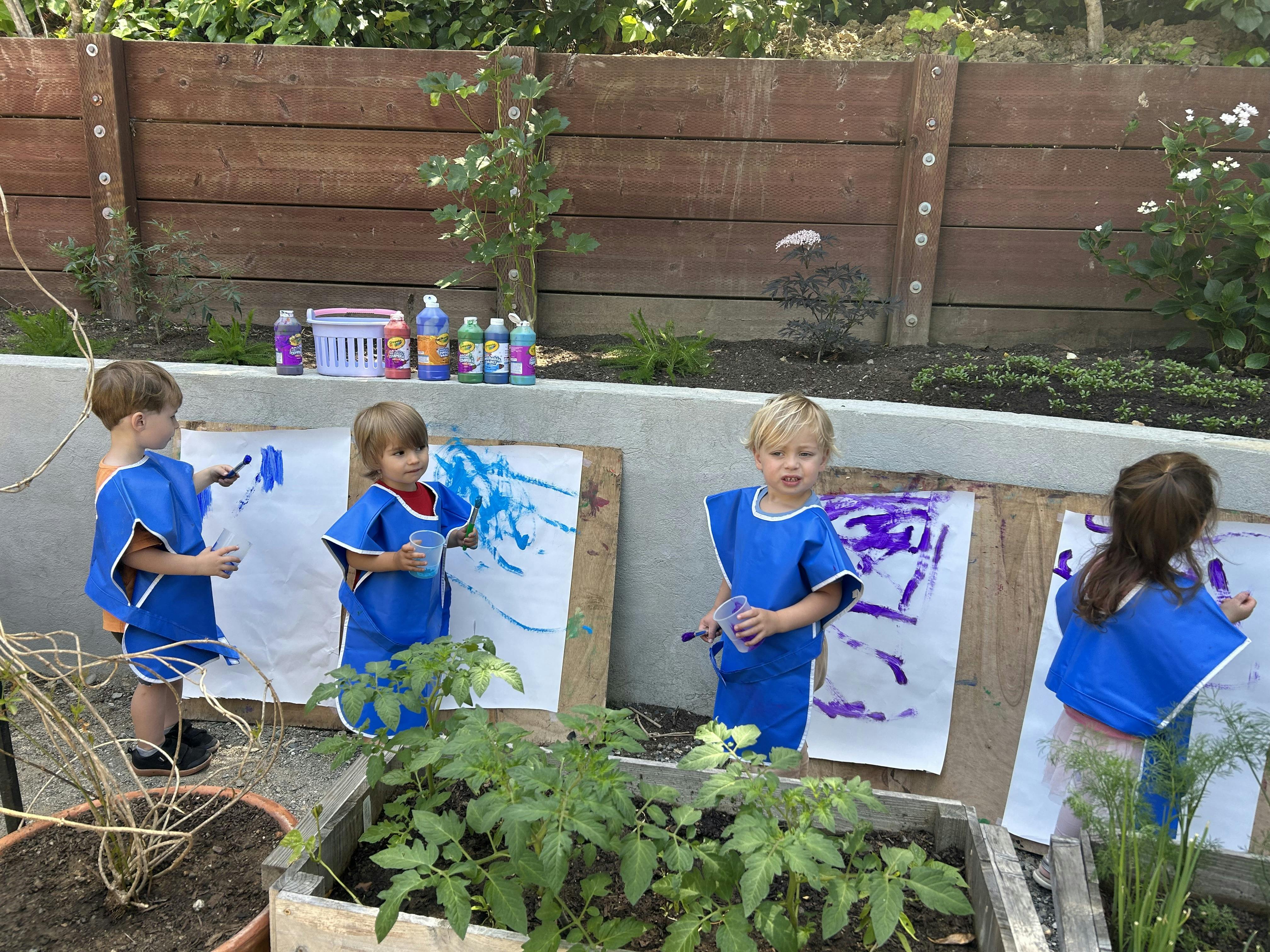 Four children painting on paper boards outdoors in a garden