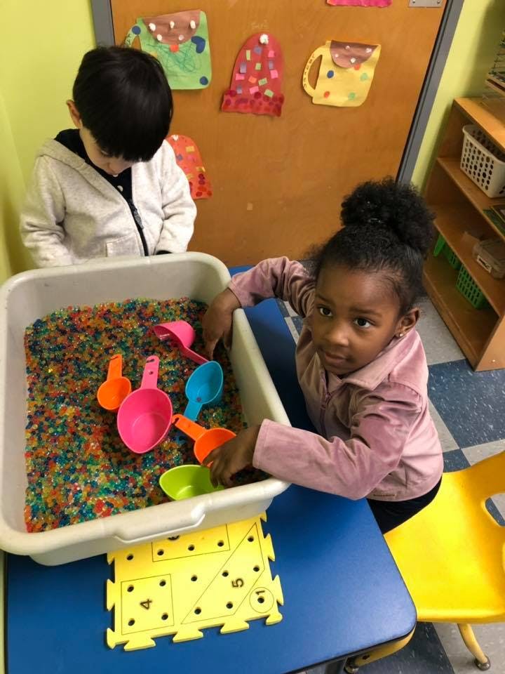 Two children playing with colorful beads and scoops in a sensory bin