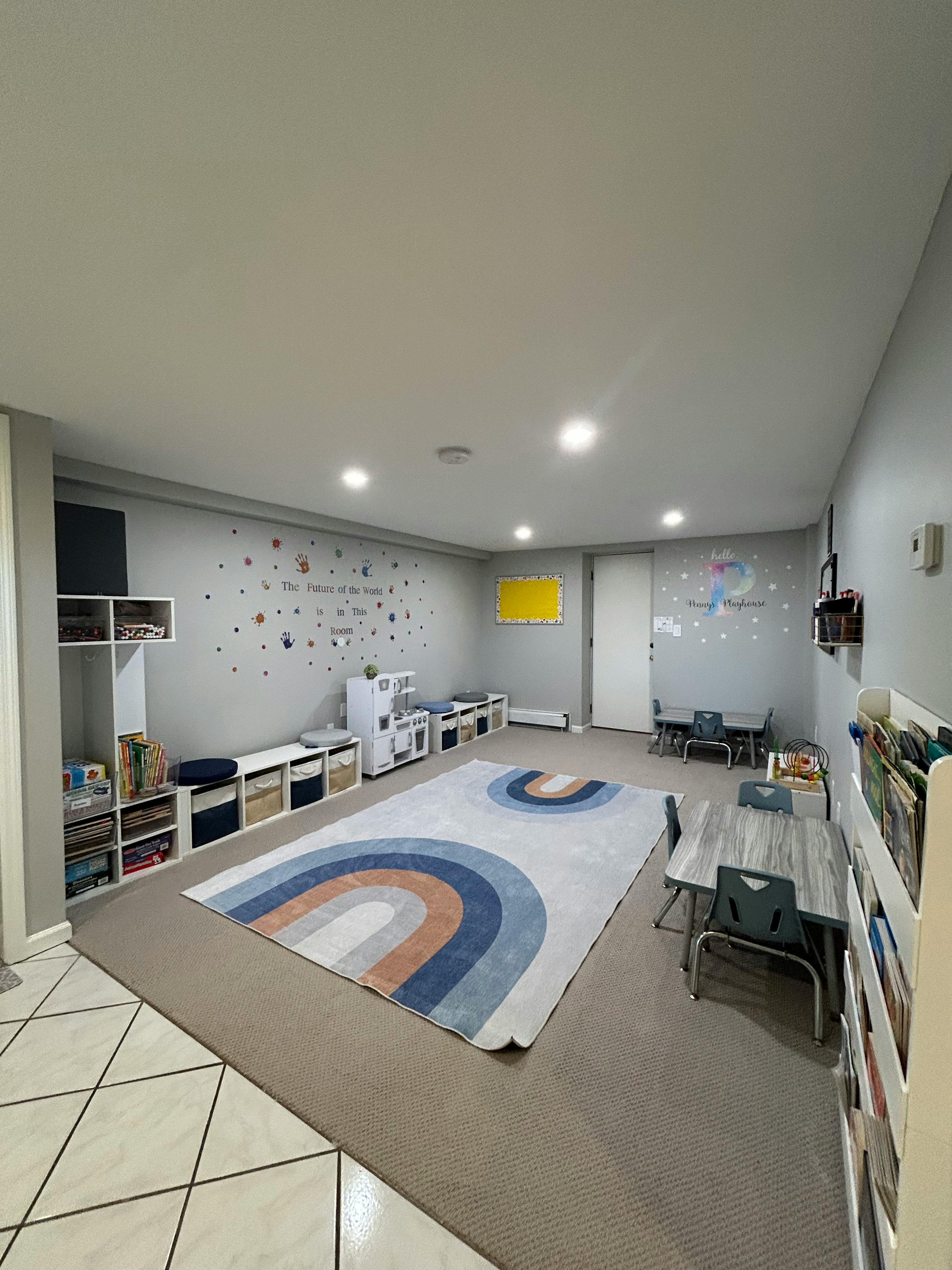 A classroom with small tables and chairs, storage units, and a rainbow rug