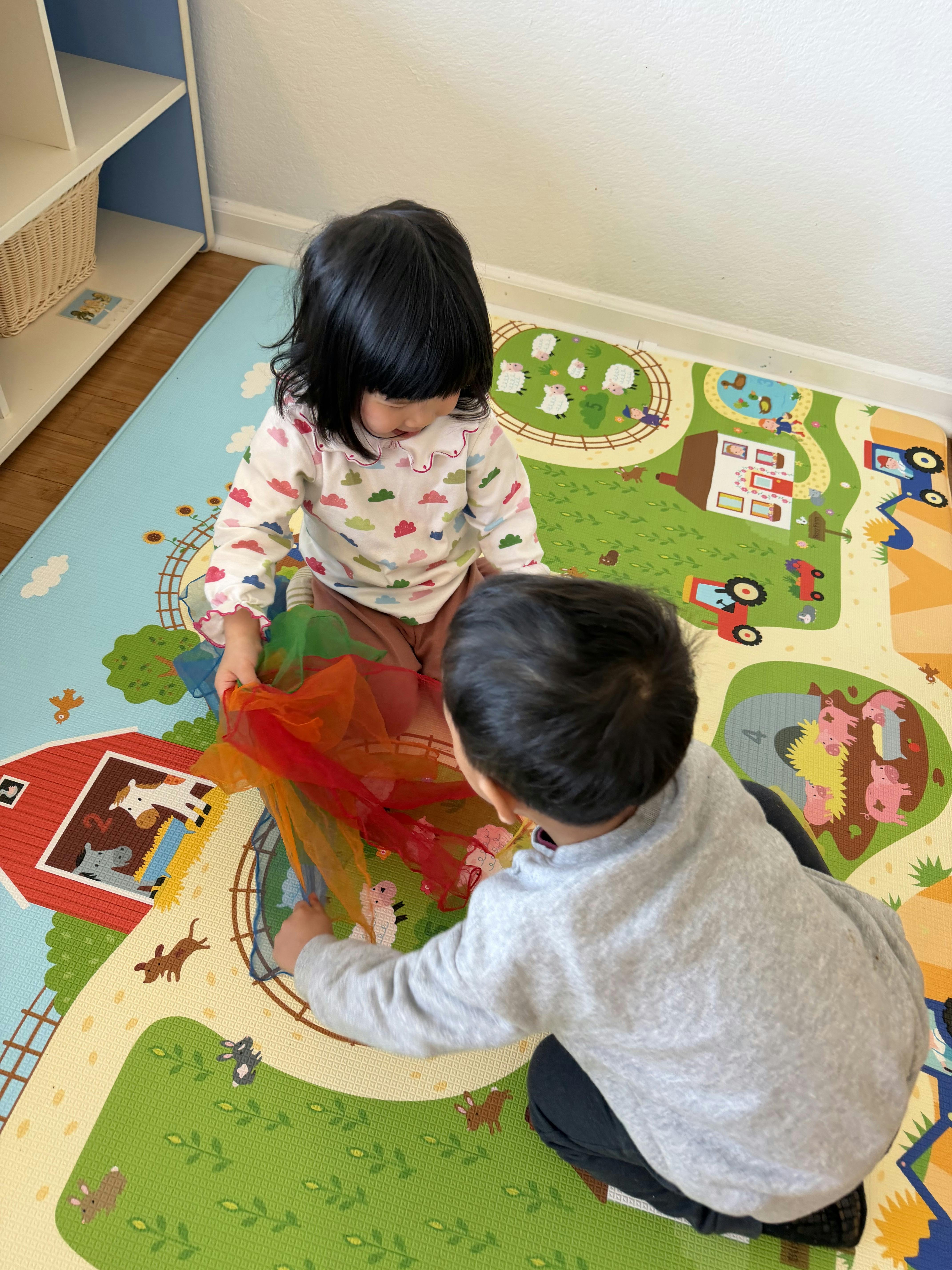 Two children playing with colorful scarves on a farm-themed playmat