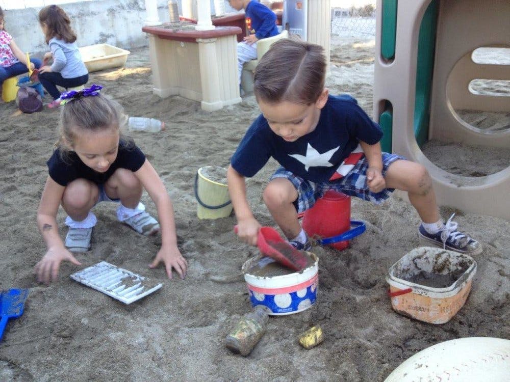 Two children playing in sand with toys