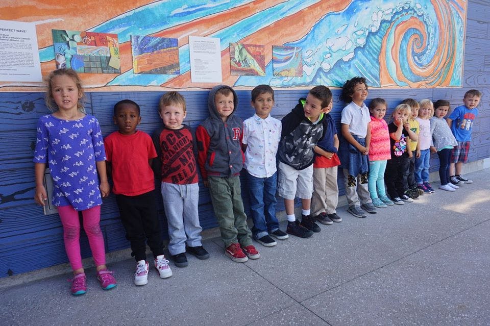 Group of children standing in a line against a colorful mural