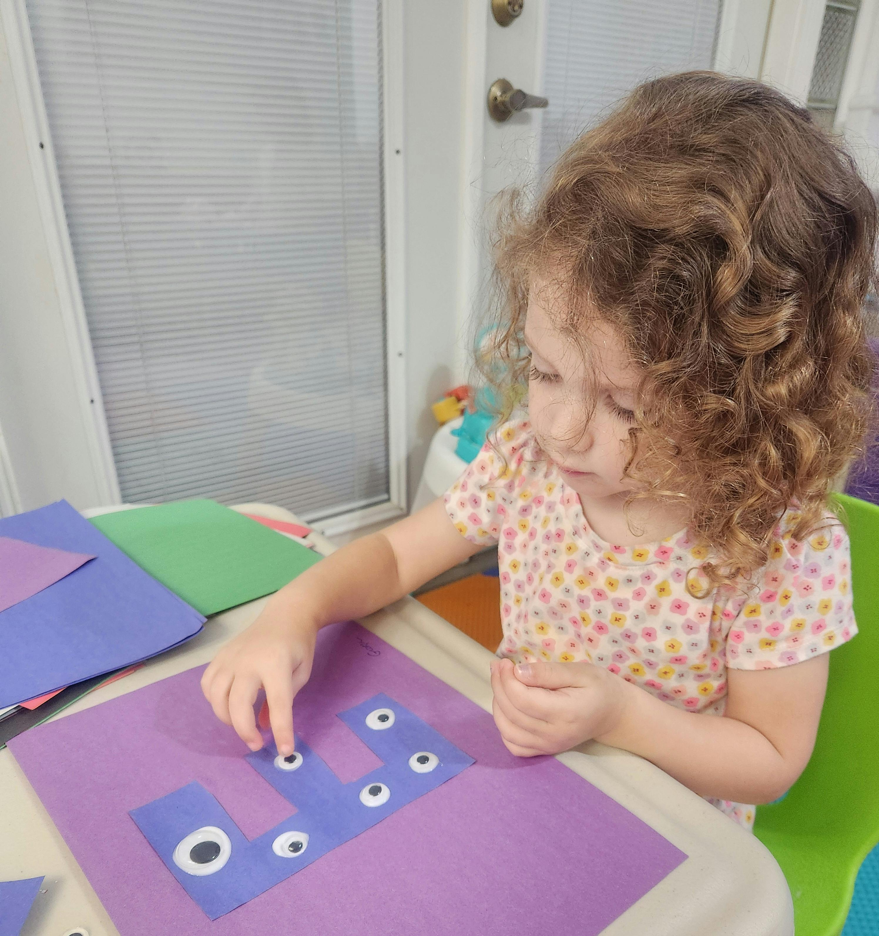 Child placing googly eyes on a purple craft paper craft