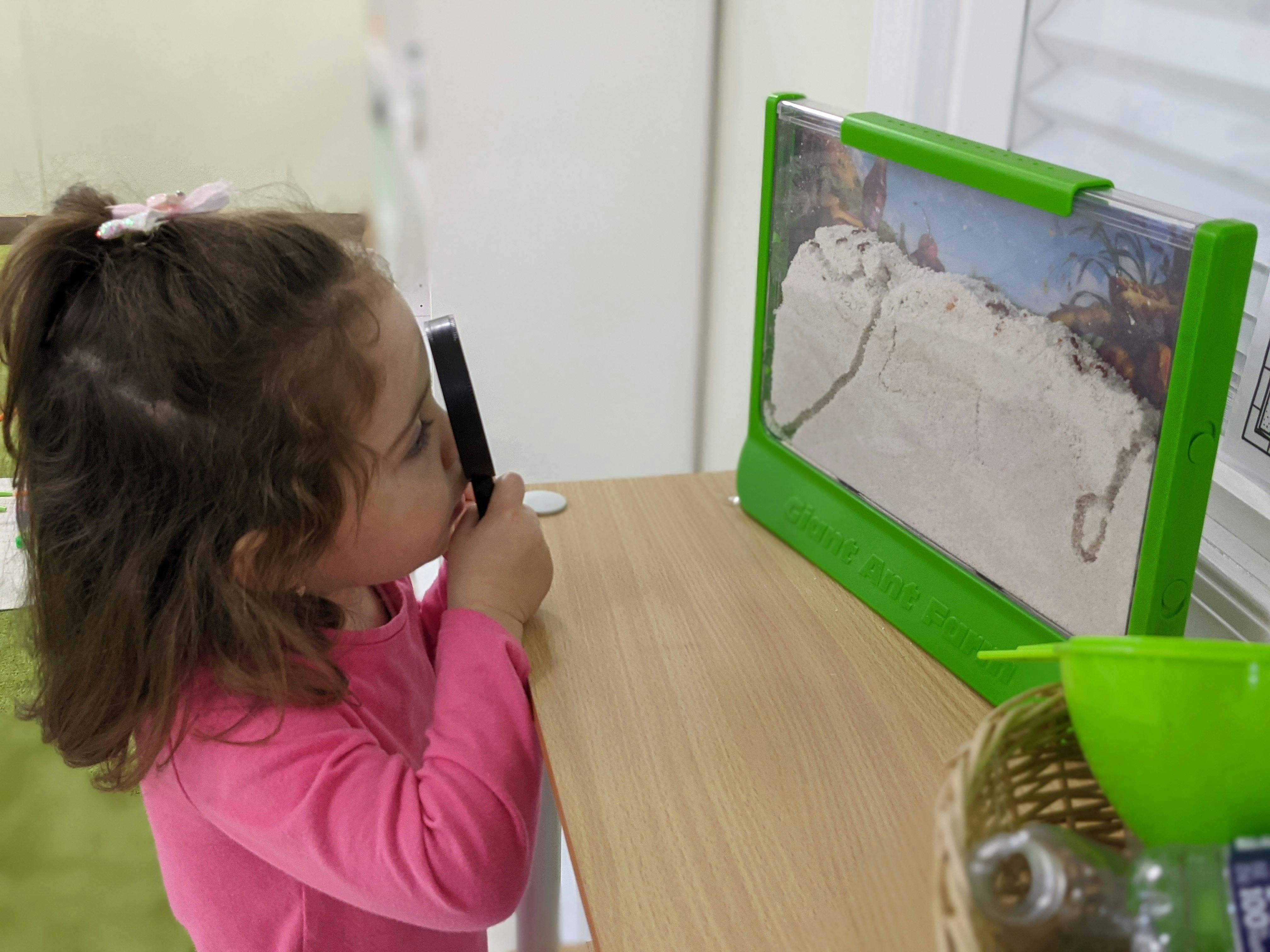 Child looking through a magnifying glass at a sand art display