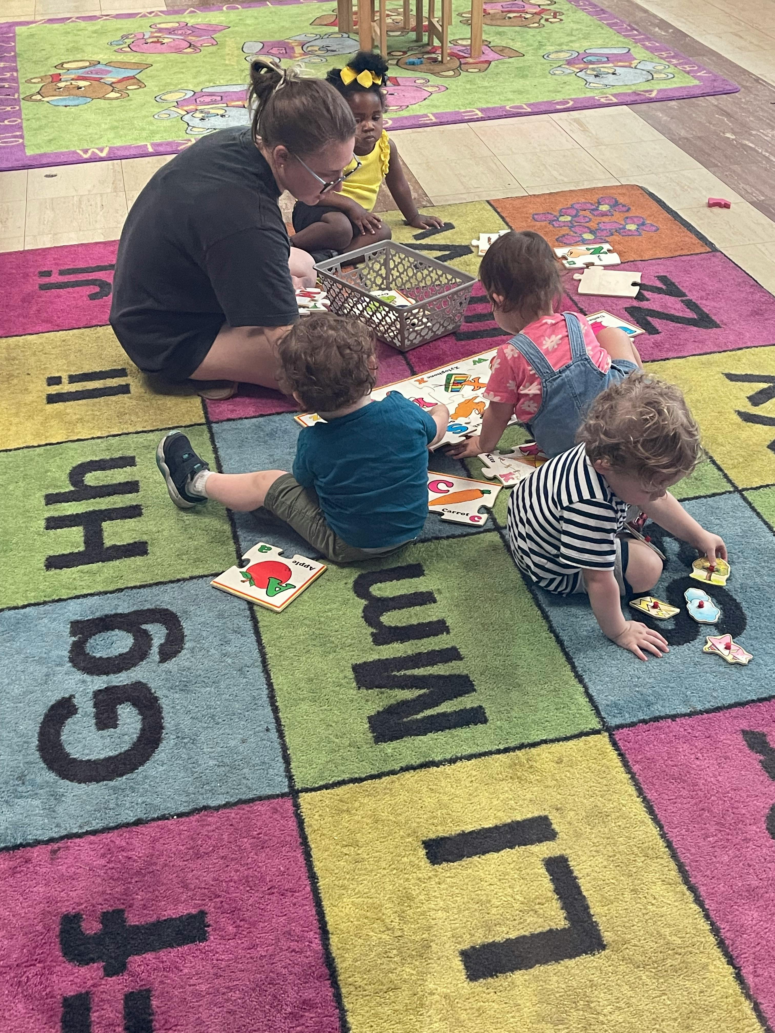 Person and three children playing with puzzles on an alphabet rug
