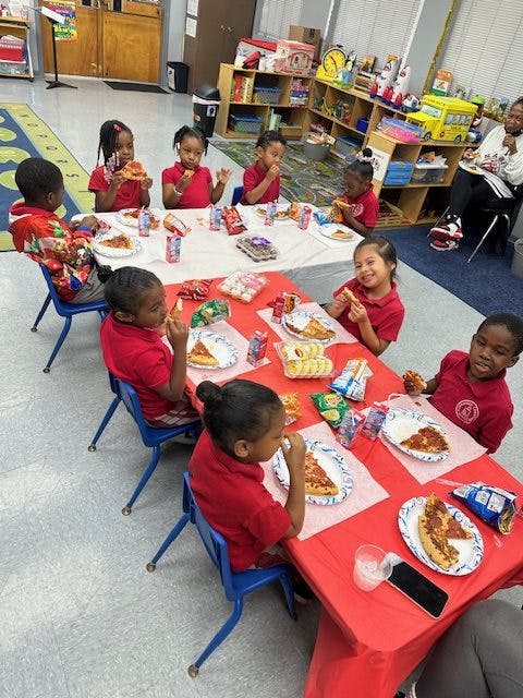 Children eating pizza at tables in a classroom
