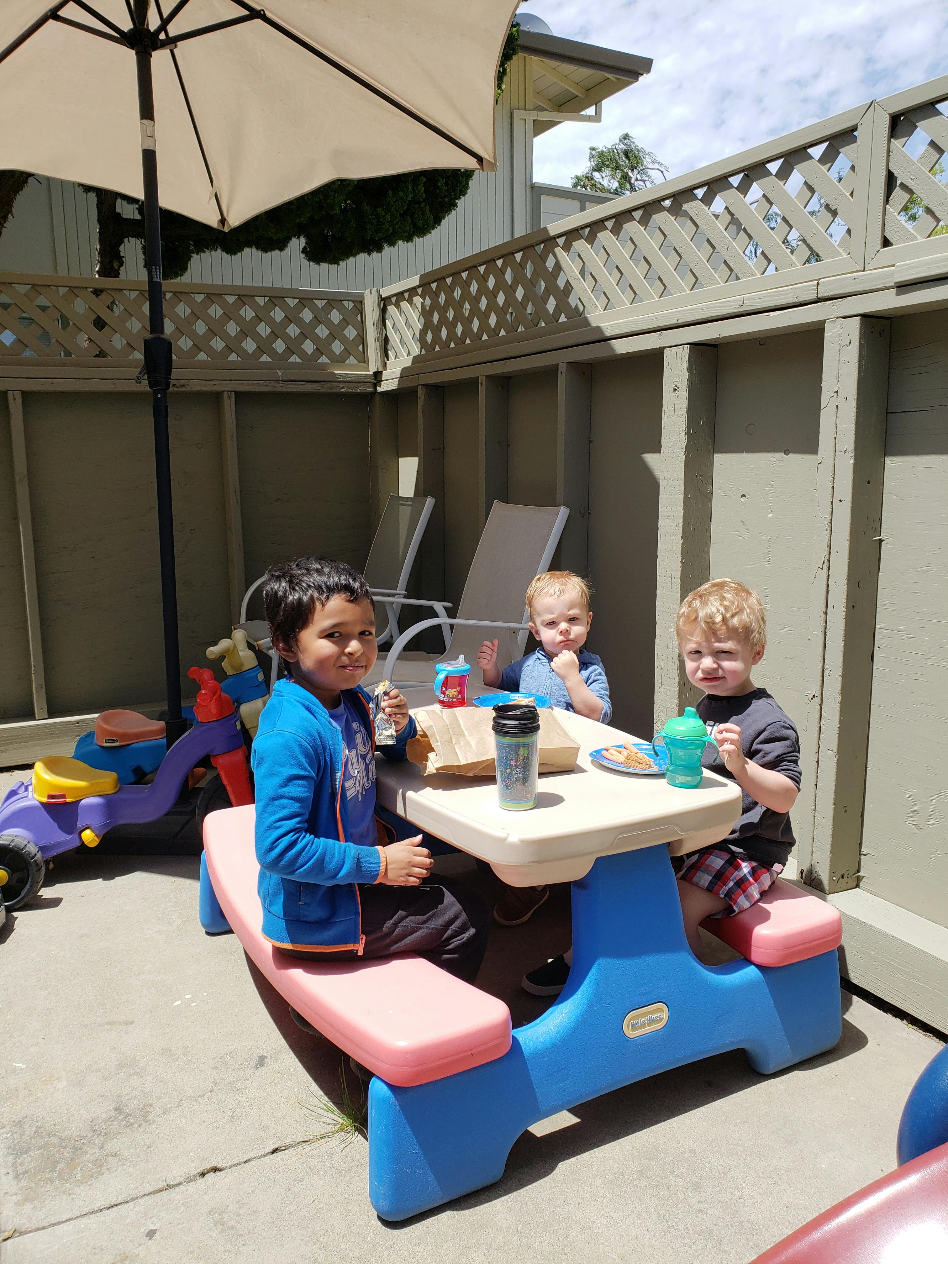 Three children sitting at a small picnic table outdoors