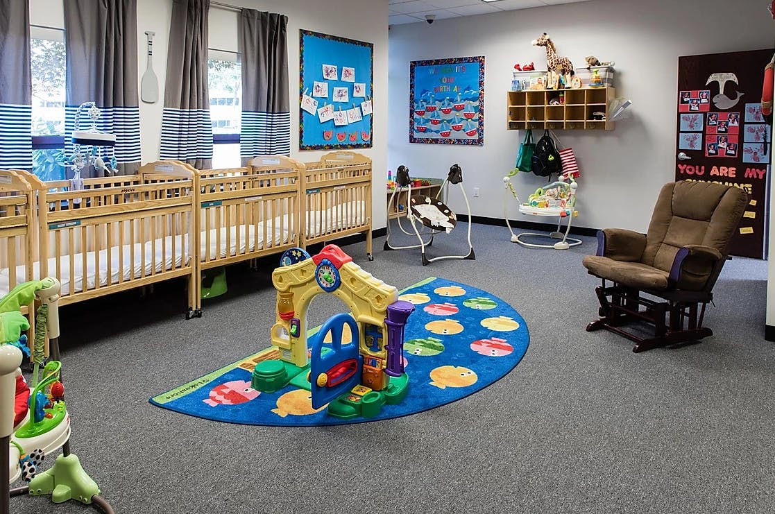 Nursery room with multiple cribs, a play mat, and a rocking chair