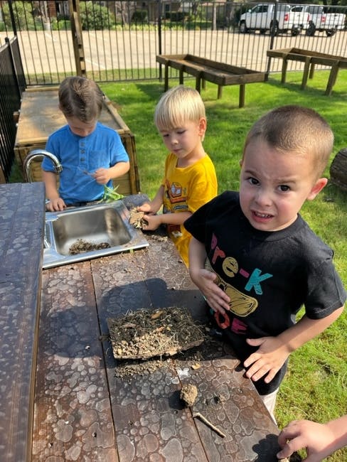 Three children playing at an outdoor sink and table