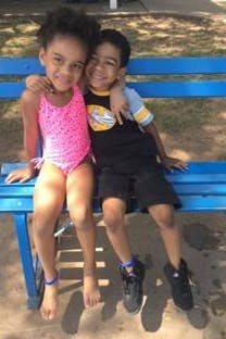 Two children sitting on a bench, one with arm around the other