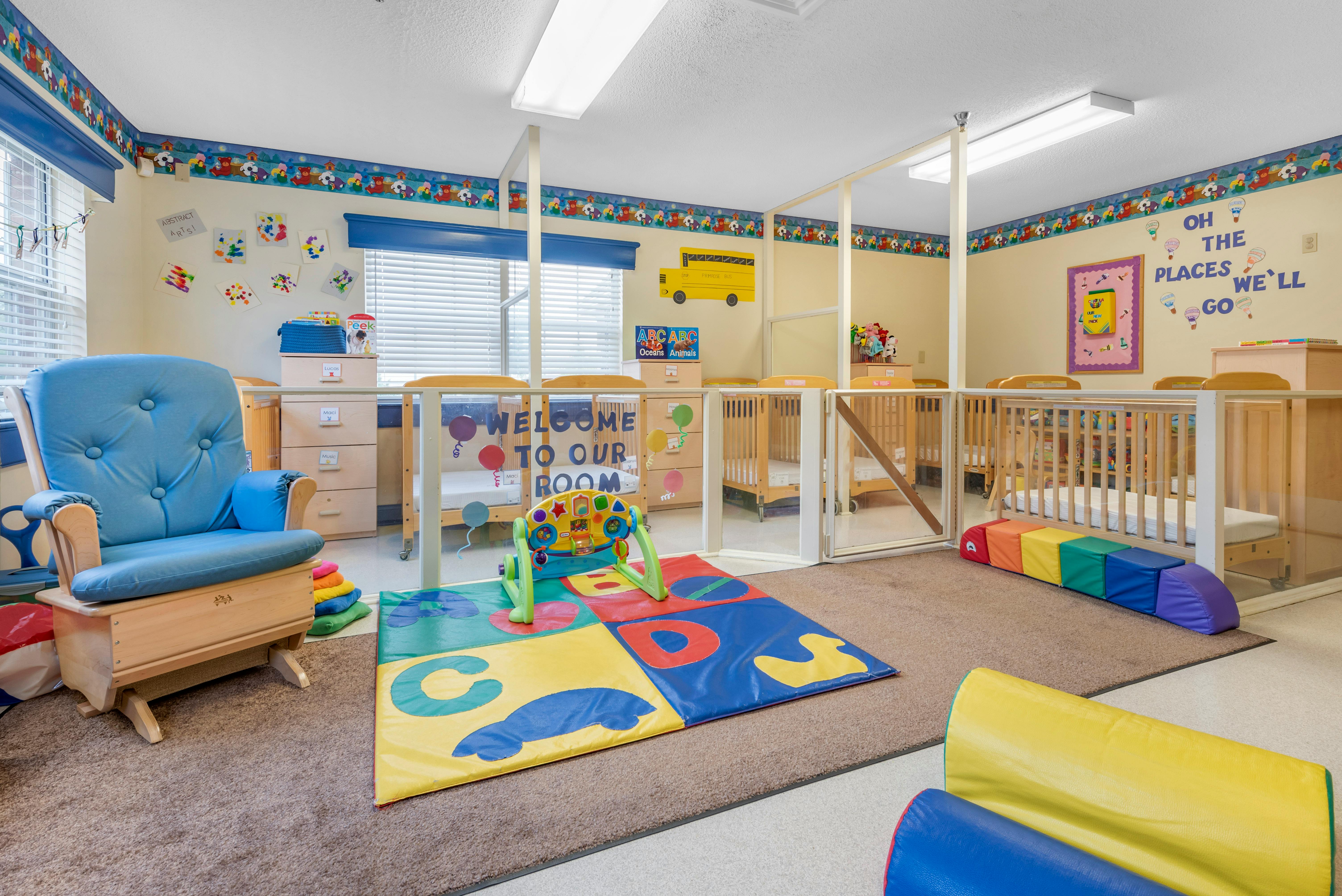Baby room with blue rocking chair, colorful play mat, and several cribs
