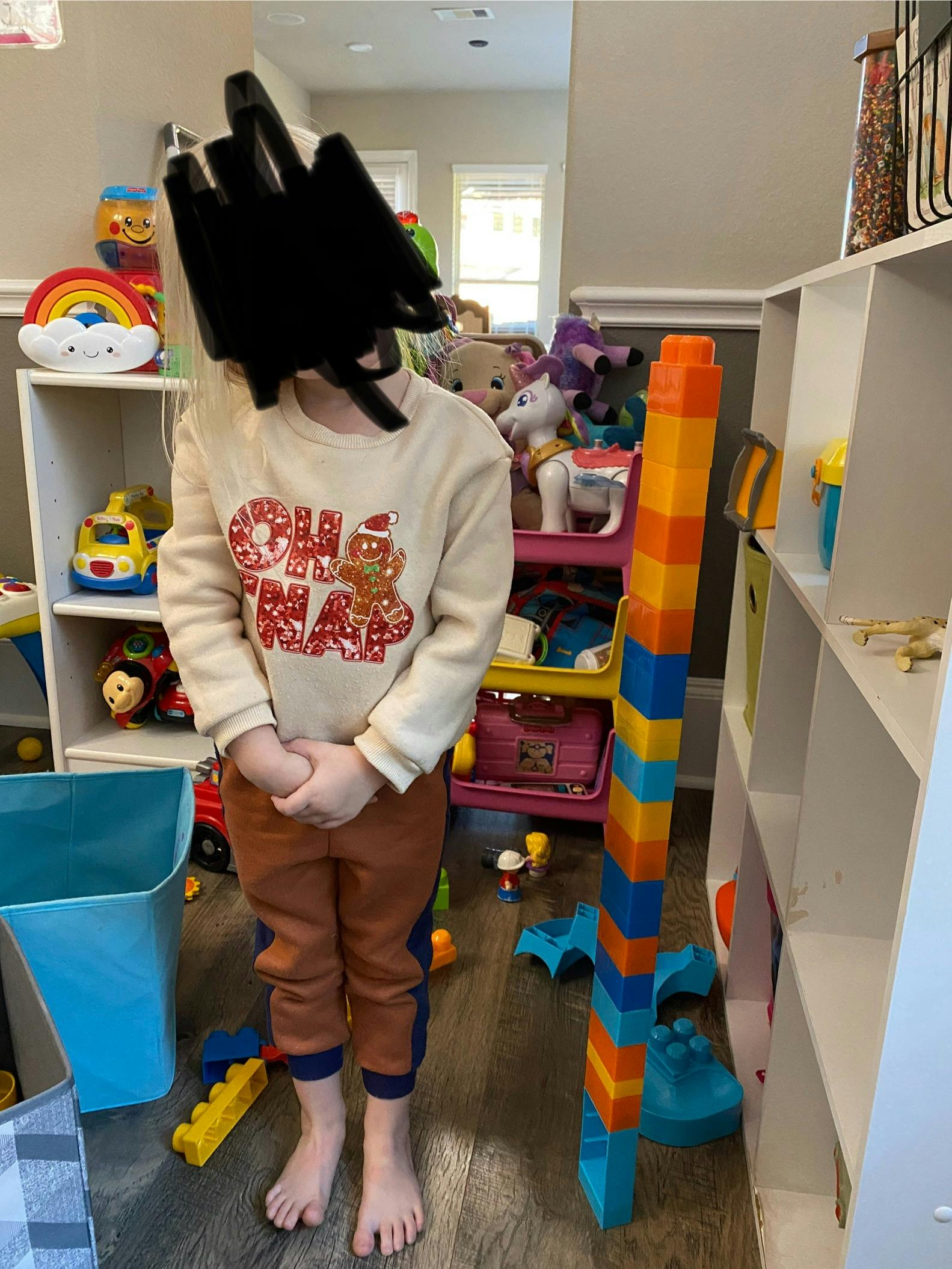 Child standing in a room with toys, wearing a shirt that says "Oh Snap"