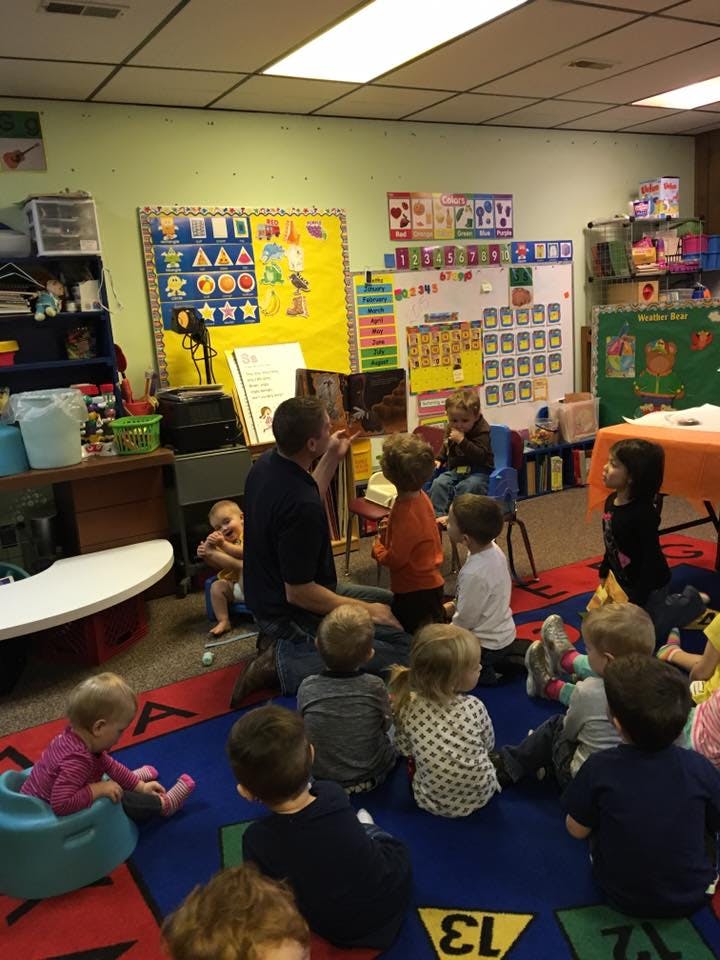 Adult reading a book to a group of children in a classroom