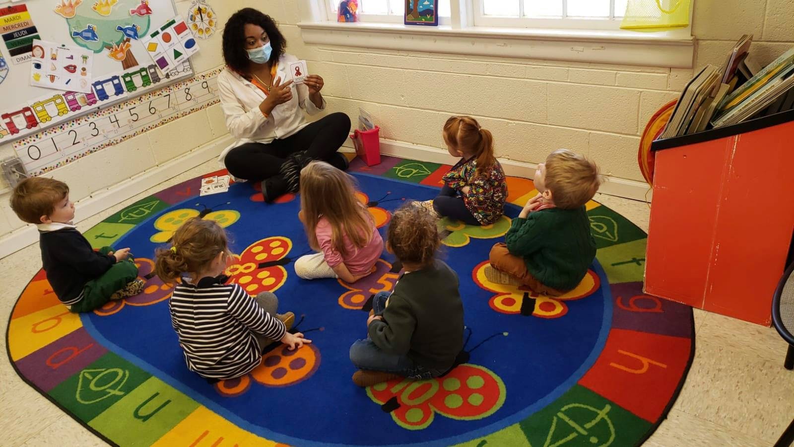 Person wearing a mask sitting on a rug with several children