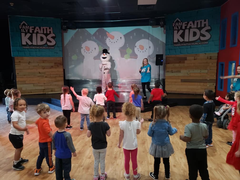 Children watching a person in a snowman costume on a stage
