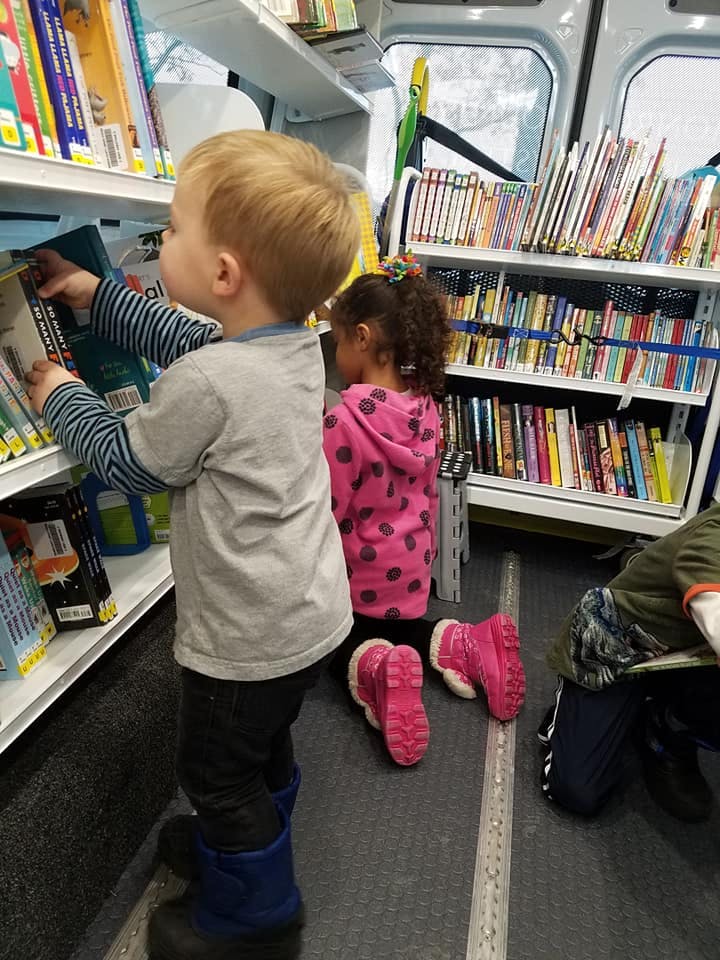 Child looking at books on a shelf, another child kneeling nearby