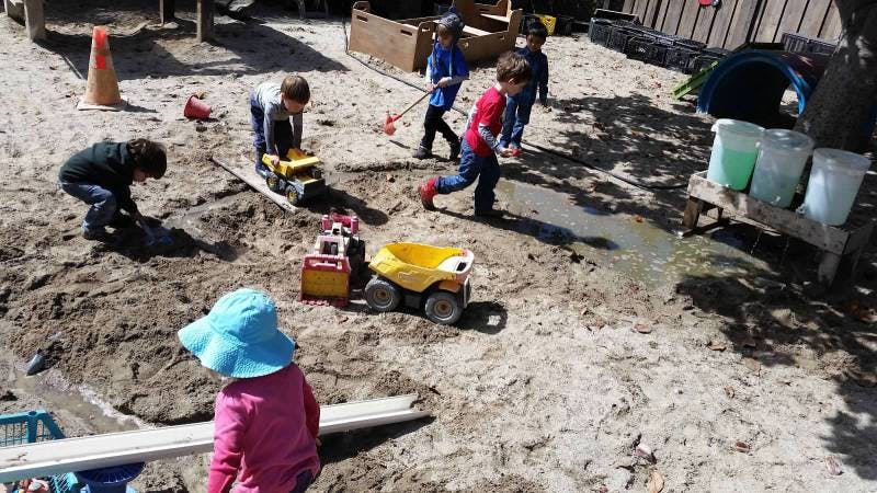 Children playing in a sandpit with toy trucks