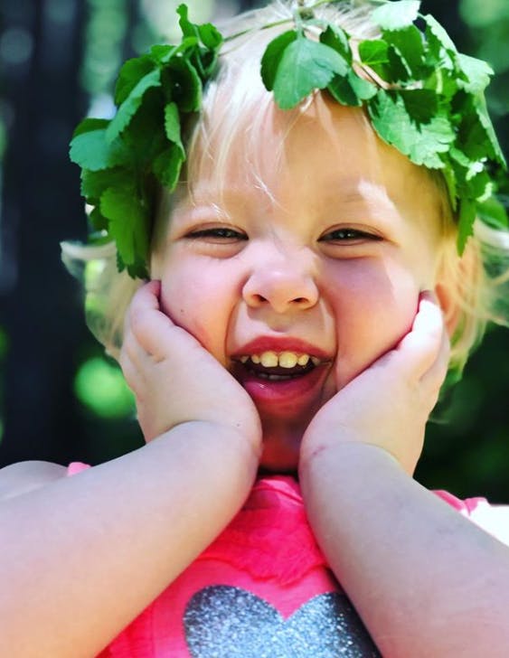 Child with a leaf crown holding hands to face