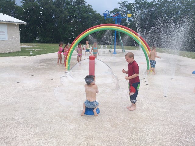 Children playing in a splash pad with a rainbow arch