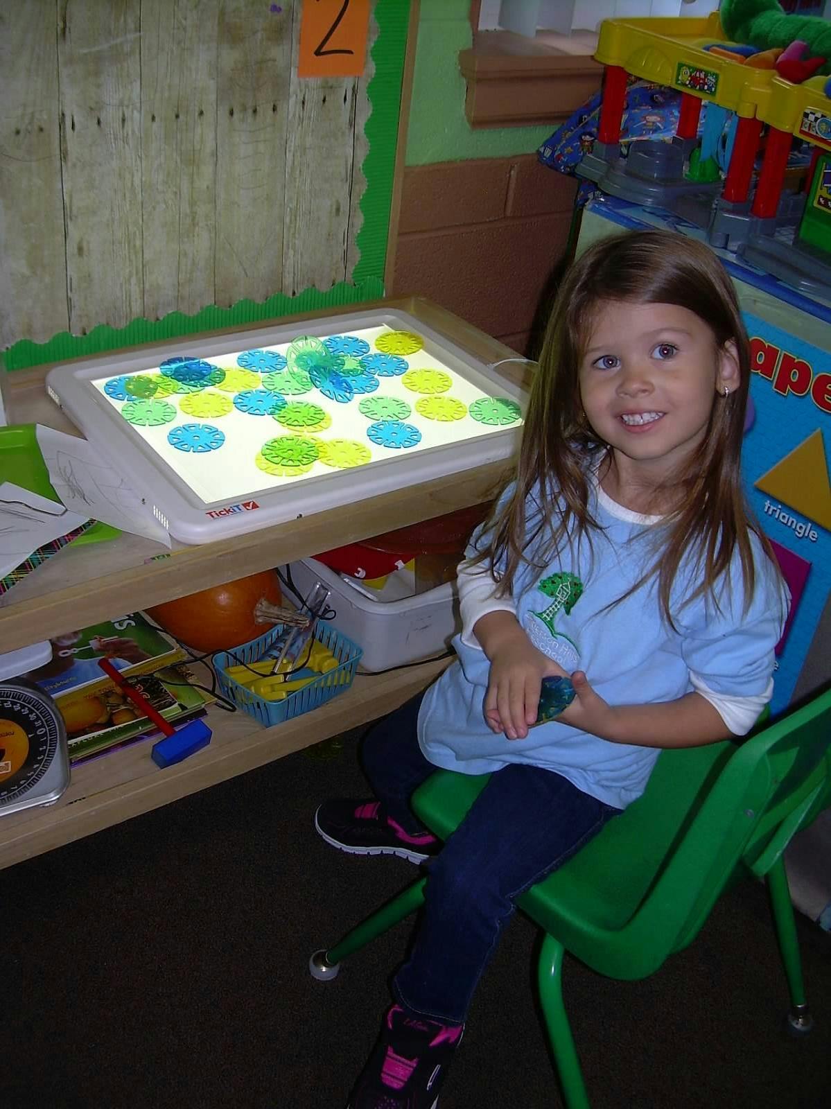 Child sitting in a chair next to a light table with colorful translucent discs