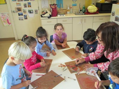 Adult and children drawing at a table in a classroom