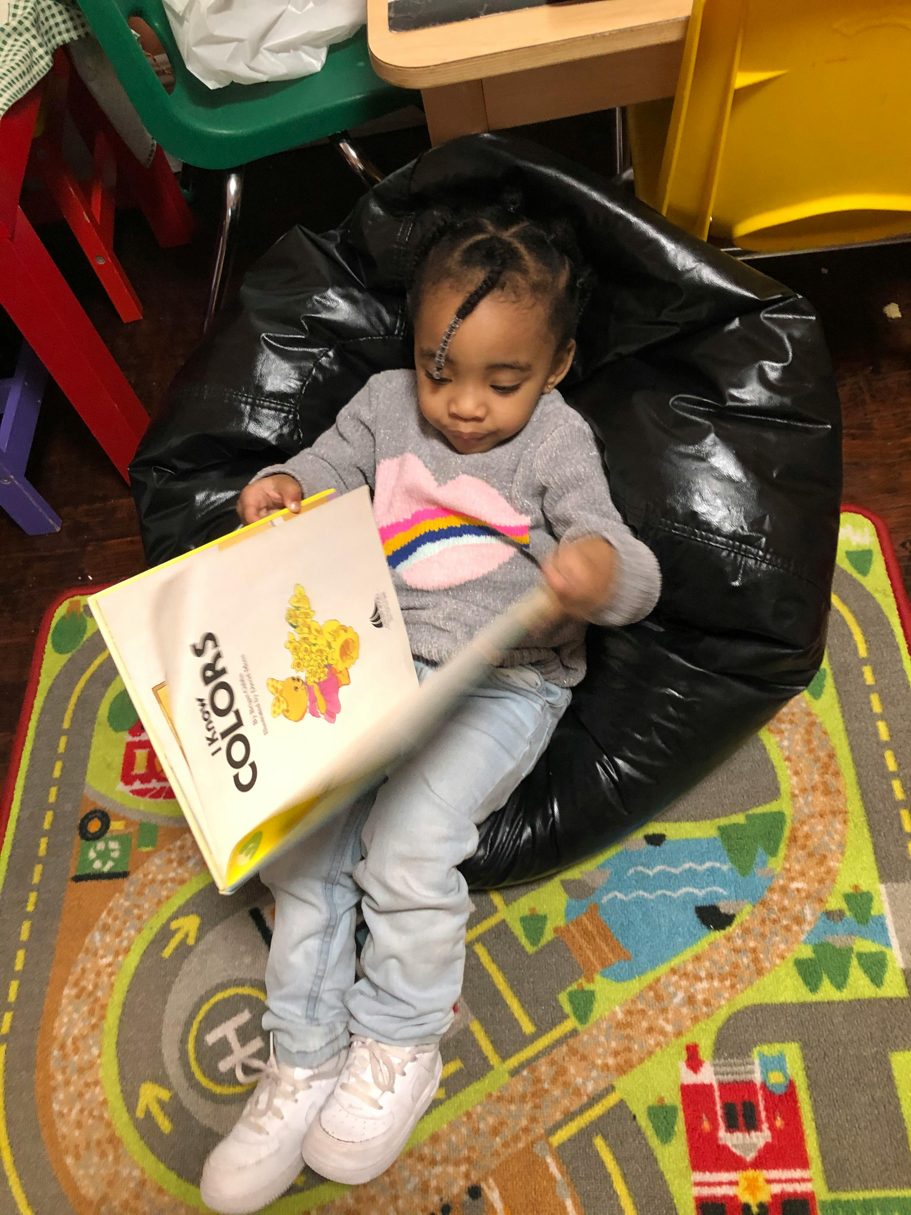 Child sitting in a beanbag chair, looking at a book titled "I Know Colors"