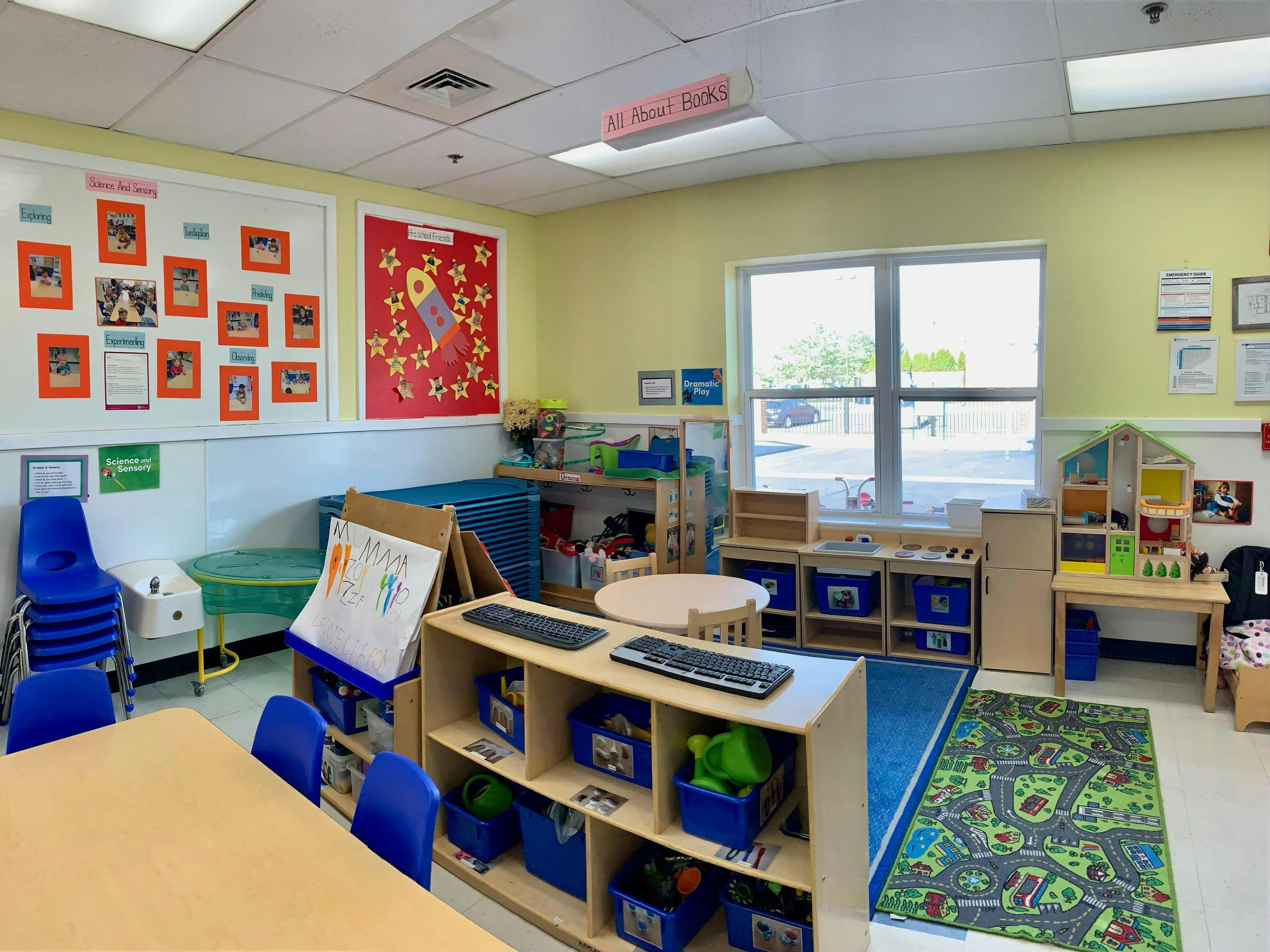 An empty classroom with bulletin boards, tables, chairs, and play areas