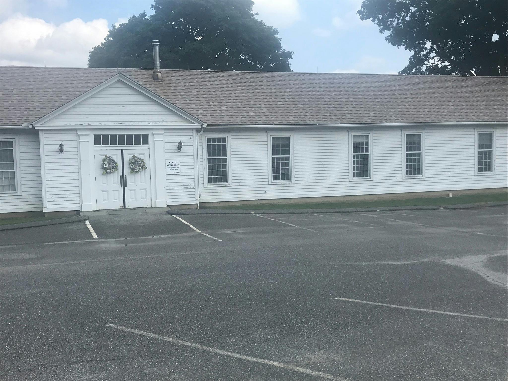 White building with a gray roof and a parking lot in front