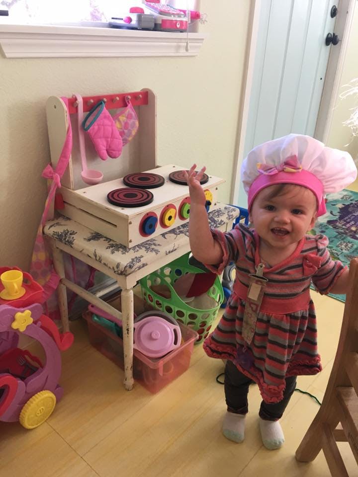 Child in a chef's hat standing next to a toy kitchen