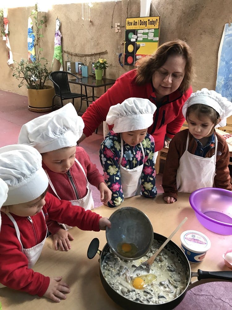Adult and three children in chef hats and aprons cooking in a classroom