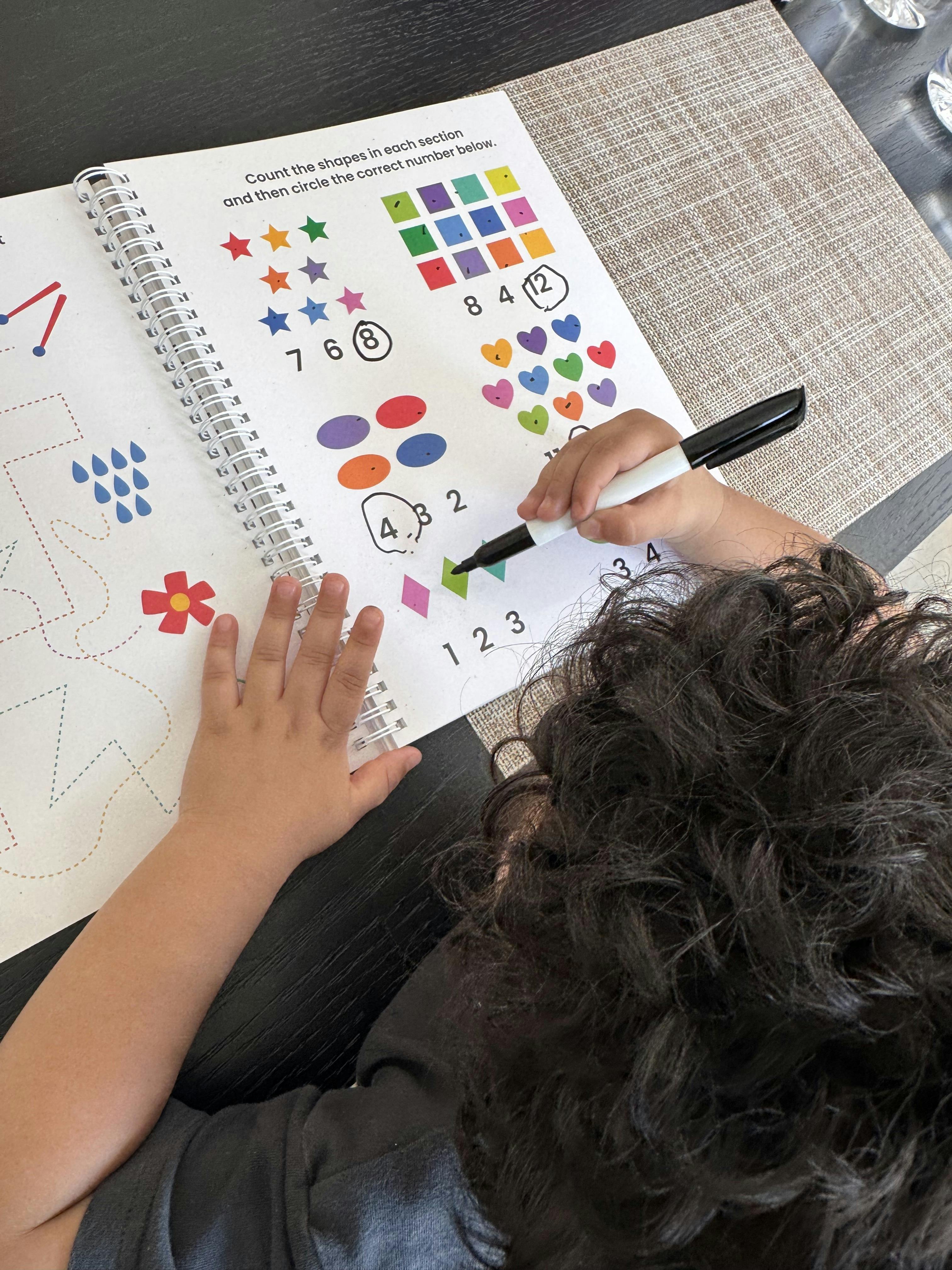 Child's hands on a workbook with shapes and numbers