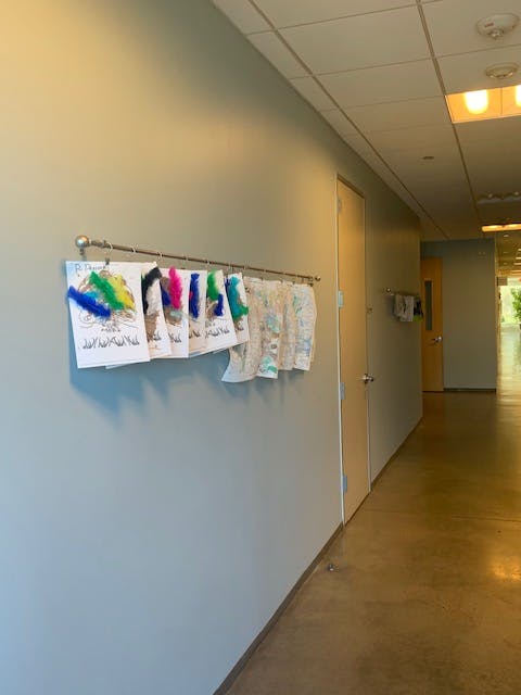 Children's artwork with feathers hanging on a wall in a hallway