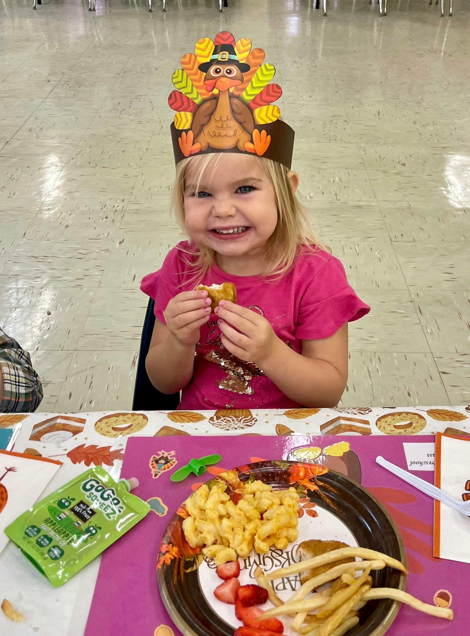 Child in a turkey hat holding food at a table with food