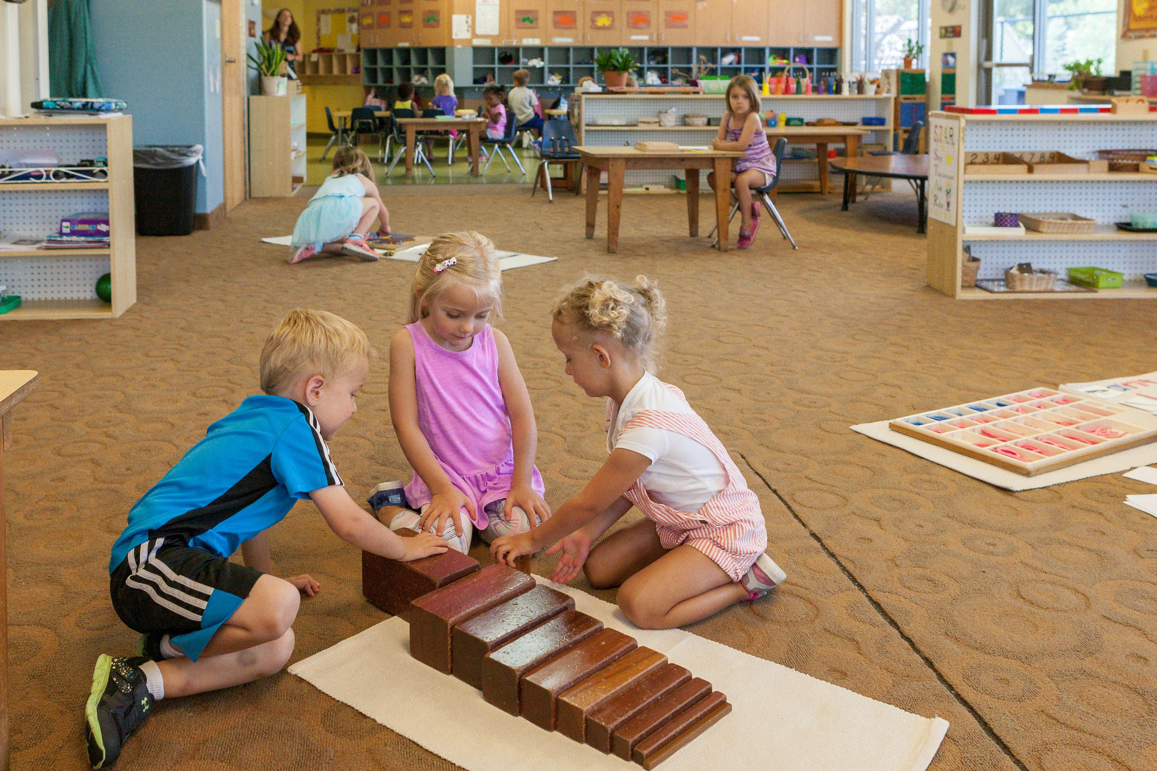 Three children playing with wooden blocks on the floor in a classroom