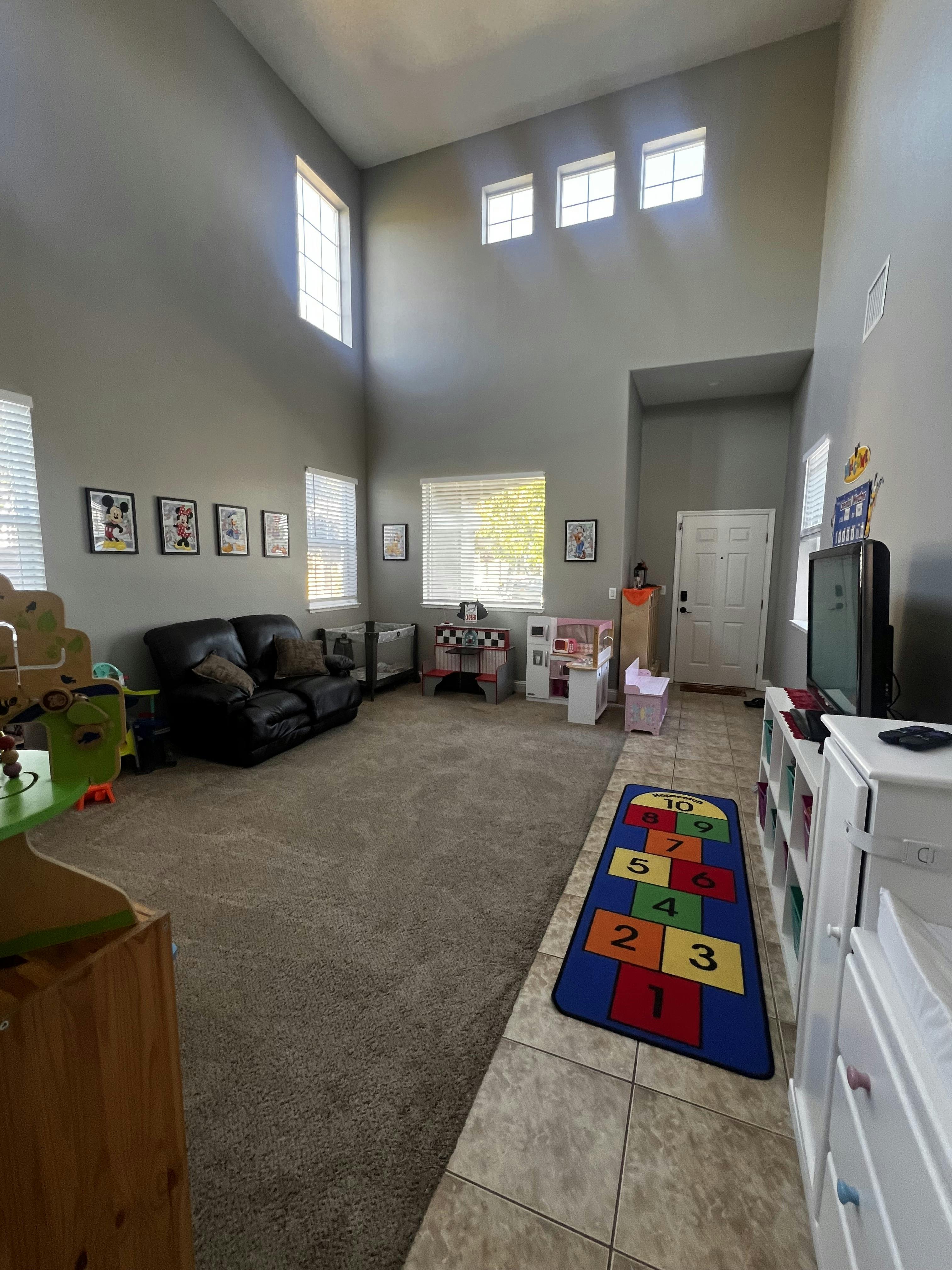 A living room with toys, a black couch, and a colorful hopscotch rug