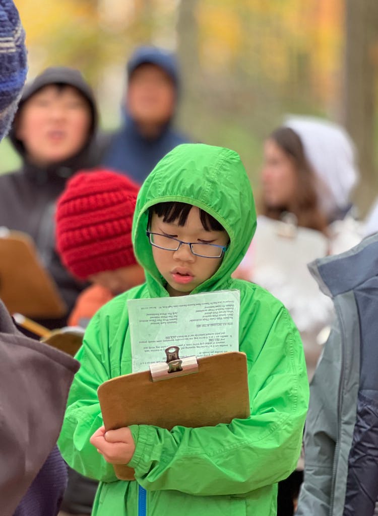Child in a green coat holding a clipboard with a worksheet