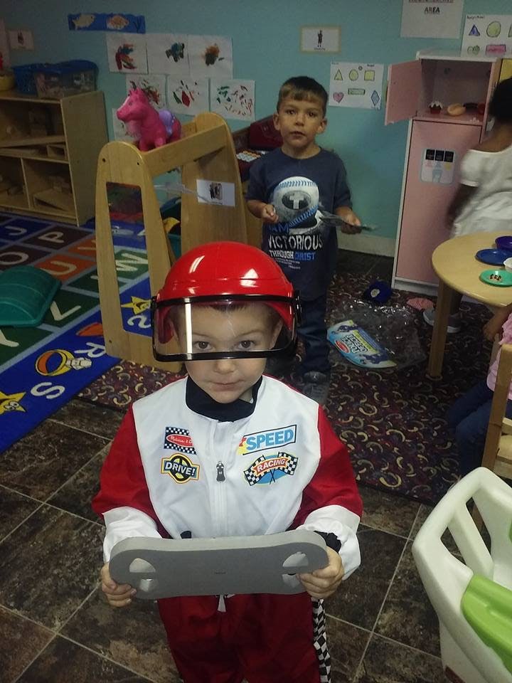 Child in a red and white race car driver costume holding a toy steering wheel