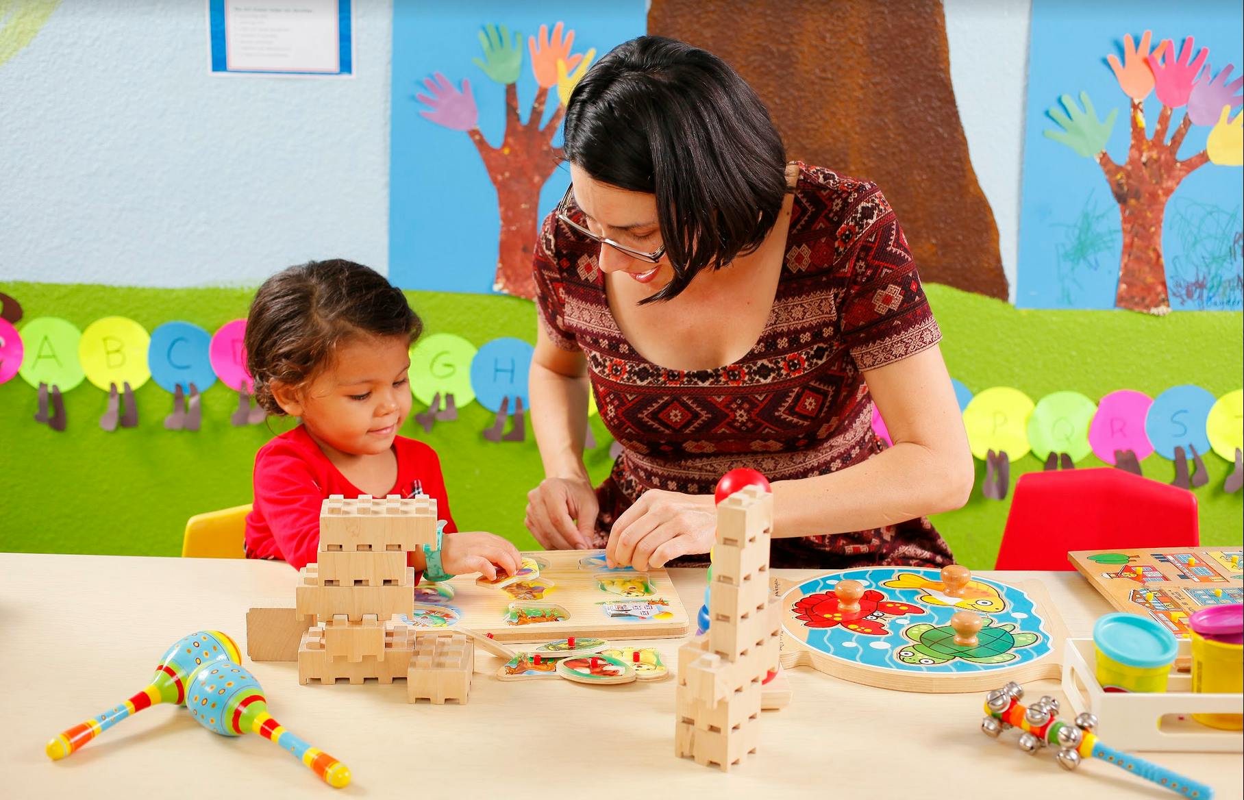 Adult and child playing with wooden blocks and puzzles at a table