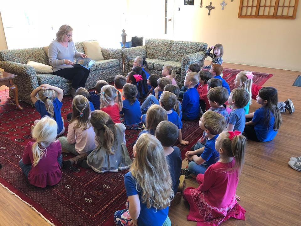 Adult reading to a group of children sitting on a rug