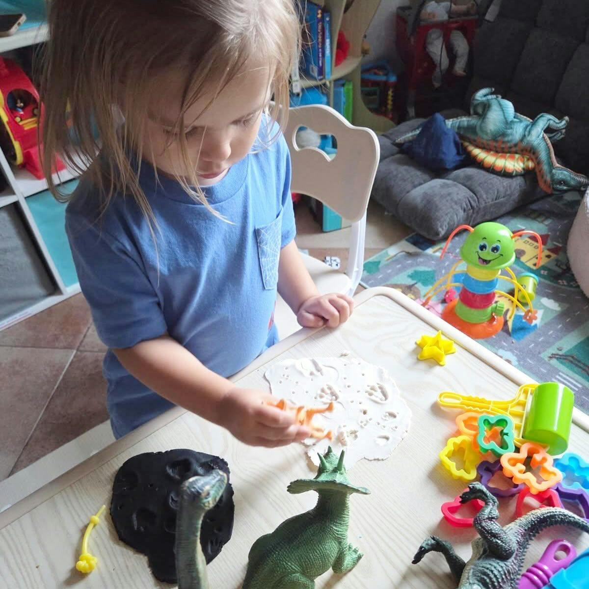 Child playing with dinosaur toys and modeling clay on a table