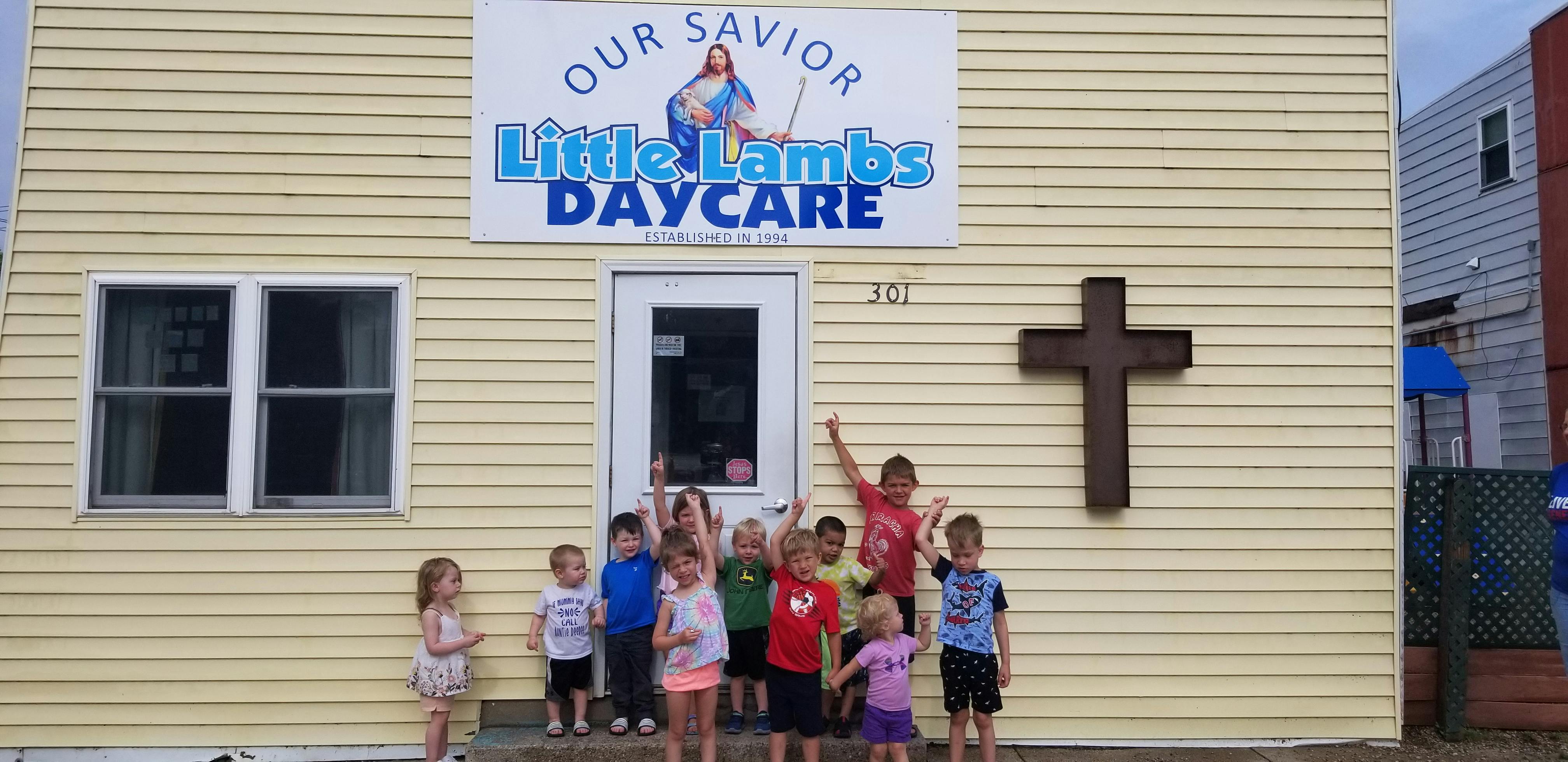 Children standing in front of a building with a sign for Little Lambs Daycare