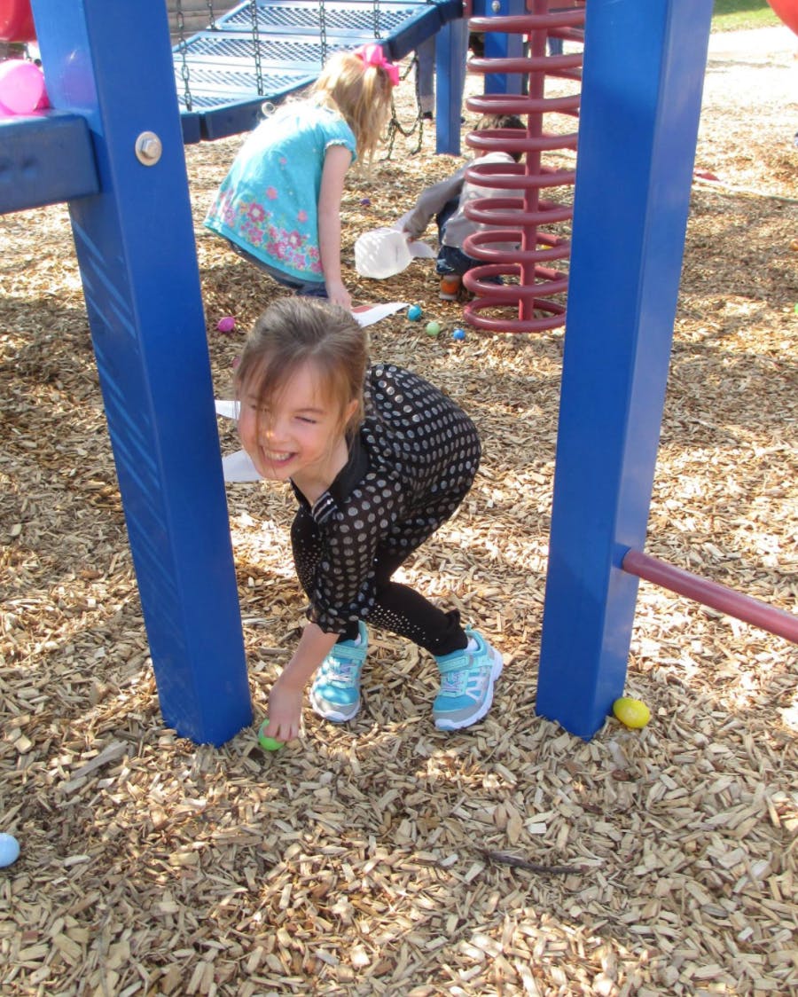 Child crouching on wood chips, reaching for an object